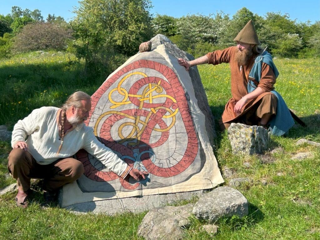 Viking guides sit beside a rune stone and explain the inscription